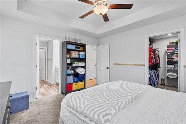 carpeted bedroom with a walk in closet, ensuite bathroom, a tray ceiling, visible vents, and a closet