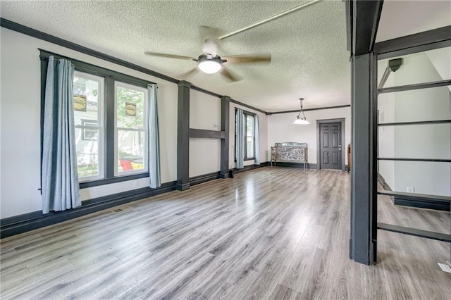 unfurnished living room with healthy amount of natural light, wood finished floors, ceiling fan, ornamental molding, and a textured ceiling