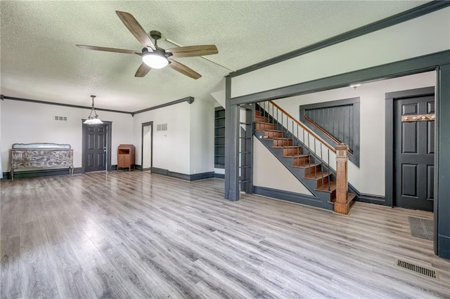 unfurnished living room with wood finished floors, a ceiling fan, stairway, a textured ceiling, and ornamental molding
