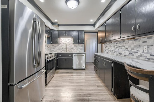 kitchen with appliances with stainless steel finishes, crown molding, a sink, light wood-type flooring, and light countertops