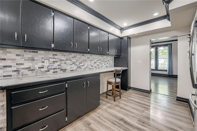 kitchen featuring light wood-type flooring, backsplash, crown molding, dark cabinetry, and baseboards