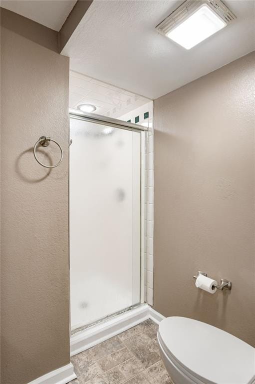 full bath with a stall shower, toilet, baseboards, and a textured wall