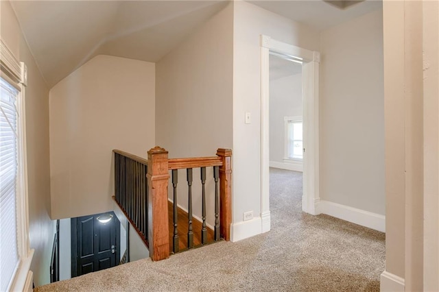 corridor with an upstairs landing, carpet, lofted ceiling, and baseboards