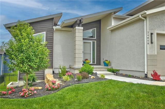 doorway to property with stucco siding, a yard, and fence