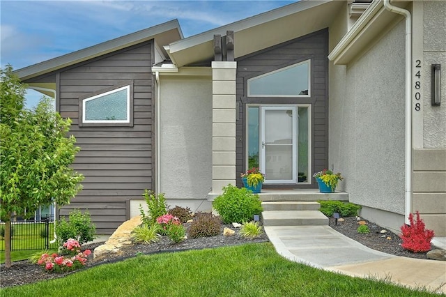 view of exterior entry with fence and stucco siding