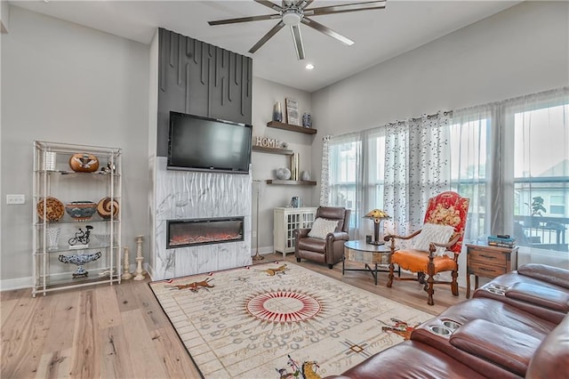 living area with wood finished floors, baseboards, recessed lighting, a large fireplace, and a ceiling fan