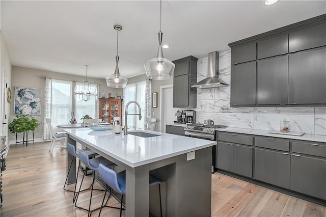 kitchen featuring a breakfast bar area, stainless steel range with gas stovetop, a sink, light countertops, and wall chimney exhaust hood