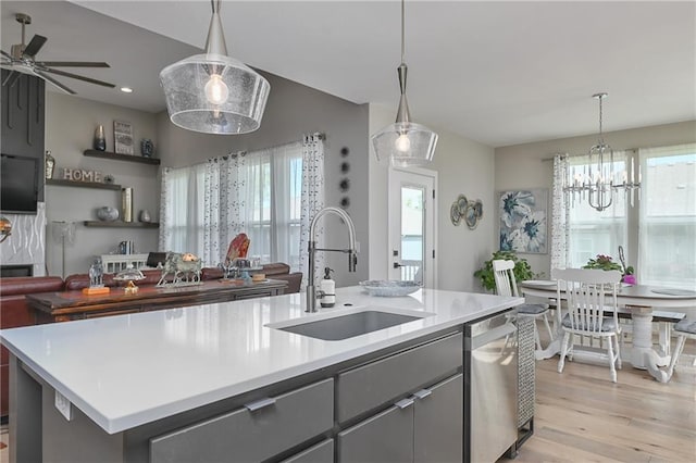 kitchen featuring a sink, ceiling fan with notable chandelier, open floor plan, stainless steel dishwasher, and gray cabinetry