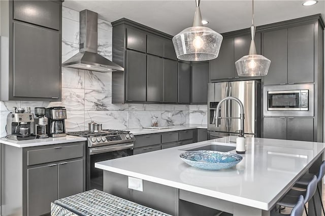 kitchen featuring gray cabinets, a kitchen bar, tasteful backsplash, stainless steel appliances, and wall chimney exhaust hood