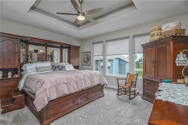 bedroom with ceiling fan, a tray ceiling, light colored carpet, and baseboards