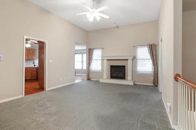 unfurnished living room featuring a fireplace, dark colored carpet, baseboards, ceiling fan, and a sink