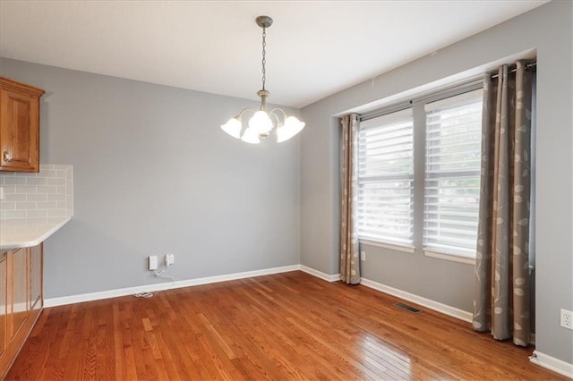 unfurnished dining area featuring an inviting chandelier, baseboards, light wood-style floors, and visible vents