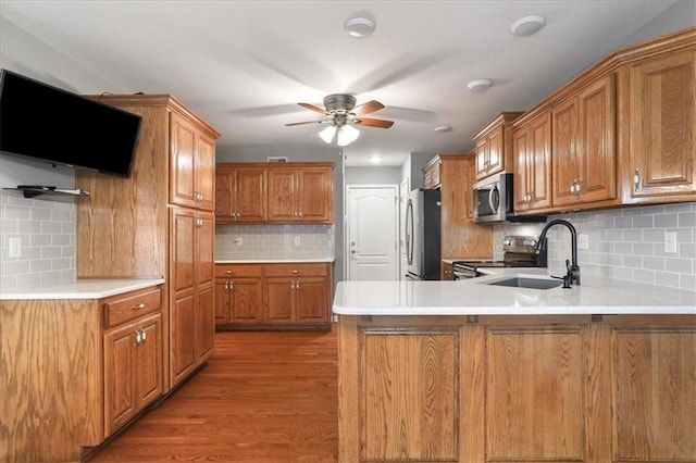 kitchen with appliances with stainless steel finishes, tasteful backsplash, brown cabinets, a sink, and a peninsula