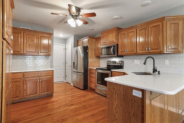 kitchen with brown cabinets, a sink, light wood finished floors, stainless steel appliances, and a peninsula
