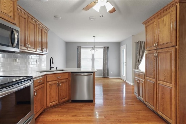 kitchen featuring brown cabinets, appliances with stainless steel finishes, a sink, a peninsula, and light wood-type flooring