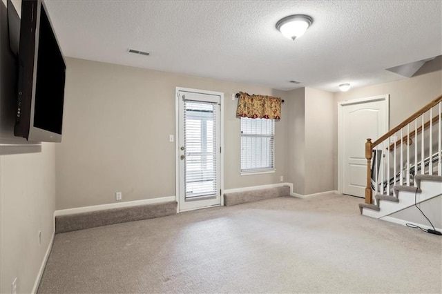 unfurnished living room with carpet floors, a textured ceiling, baseboards, and stairway