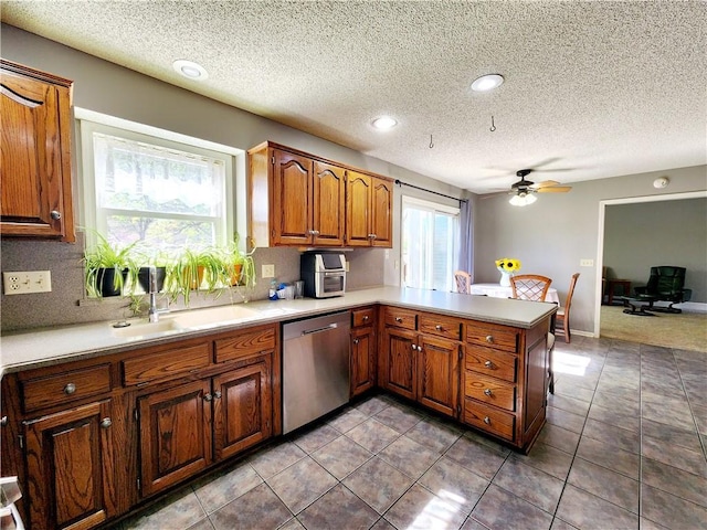 kitchen with a textured ceiling, a ceiling fan, brown cabinets, stainless steel dishwasher, and a sink