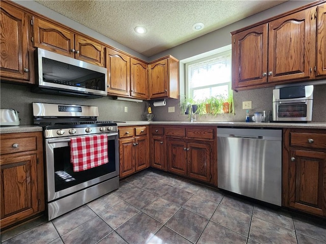 kitchen with dark tile patterned flooring, brown cabinets, appliances with stainless steel finishes, and a textured ceiling