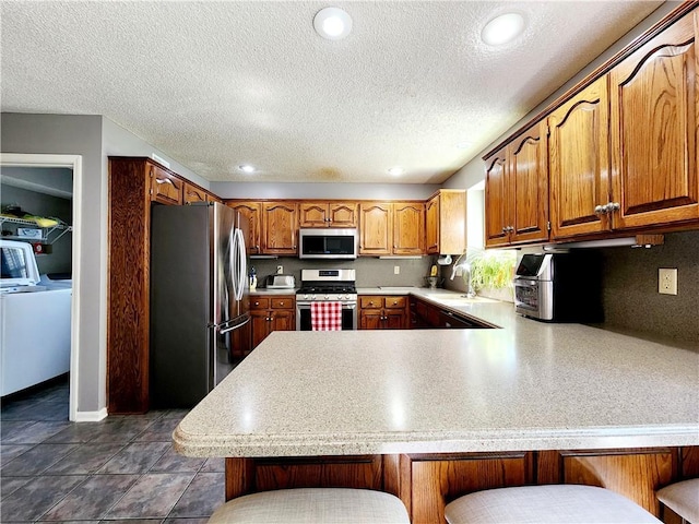 kitchen featuring a peninsula, light countertops, a breakfast bar area, stainless steel appliances, and a sink