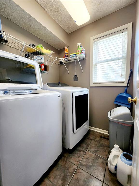 laundry room featuring dark tile patterned floors, baseboards, washing machine and dryer, a textured ceiling, and laundry area