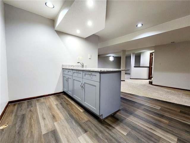 kitchen with gray cabinetry, a peninsula, dark wood-style flooring, and baseboards