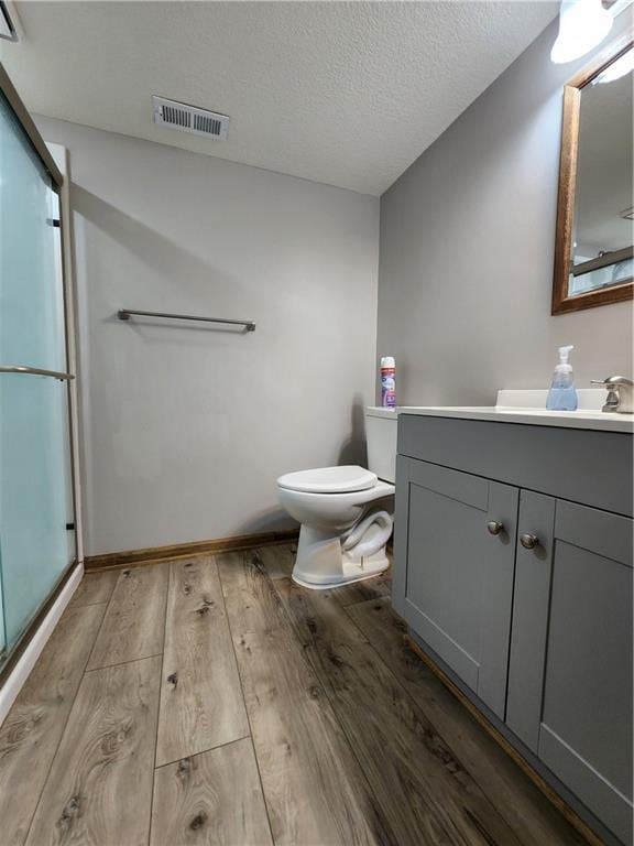 bathroom featuring visible vents, toilet, hardwood / wood-style flooring, a shower stall, and vanity