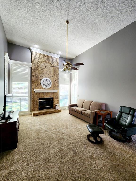 carpeted living room with a fireplace, a textured ceiling, and ceiling fan