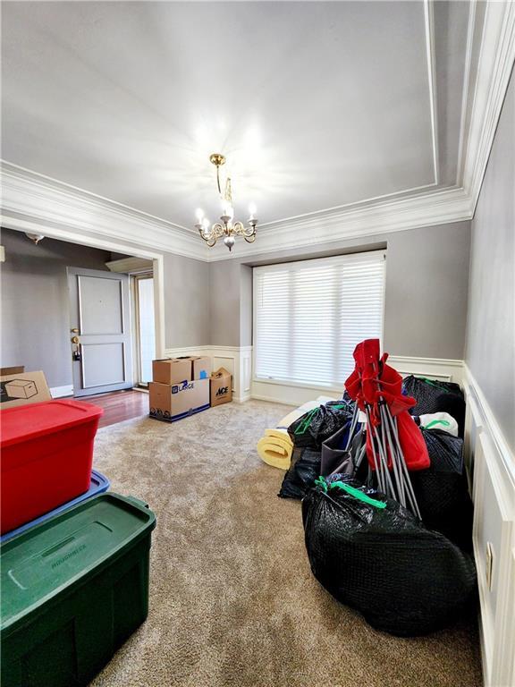 playroom featuring an inviting chandelier, carpet flooring, crown molding, a wainscoted wall, and a decorative wall