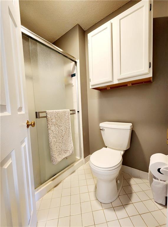 bathroom with baseboards, tile patterned flooring, a textured ceiling, toilet, and a shower stall