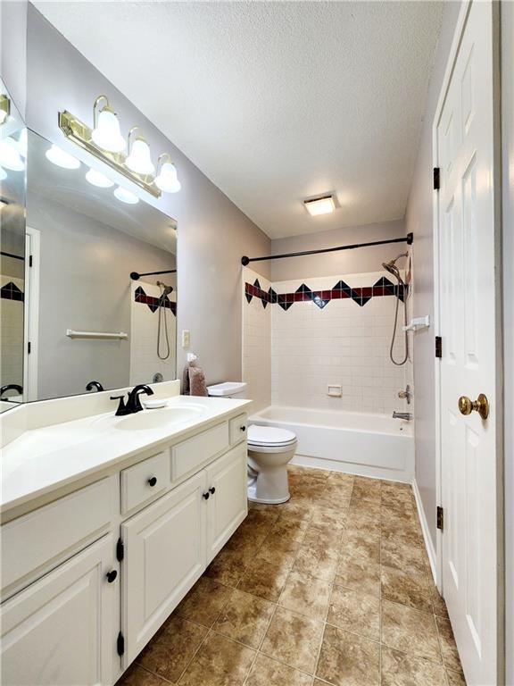 full bathroom with bathing tub / shower combination, vanity, a textured ceiling, and toilet