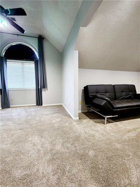 interior space featuring a textured ceiling, ceiling fan, carpet flooring, and vaulted ceiling