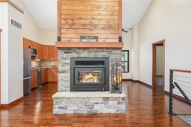 interior space featuring stainless steel appliances, wood finished floors, visible vents, a stone fireplace, and baseboards