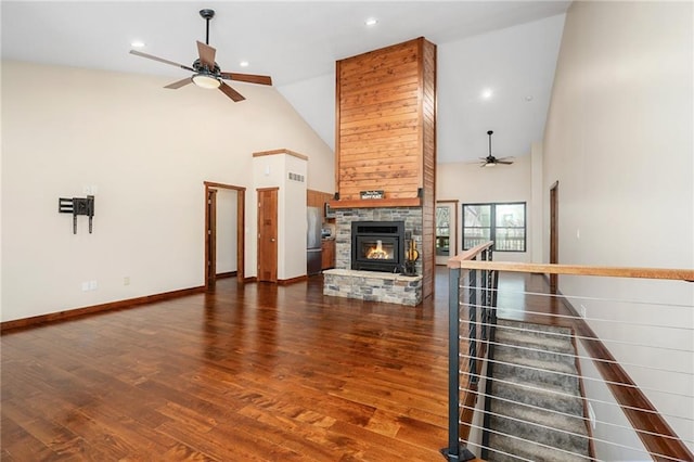 unfurnished living room with a stone fireplace, wood finished floors, high vaulted ceiling, and ceiling fan