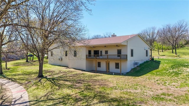 back of property with ceiling fan, a chimney, a yard, and stucco siding