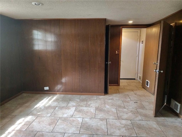 spare room featuring a textured ceiling, visible vents, wood walls, and baseboards