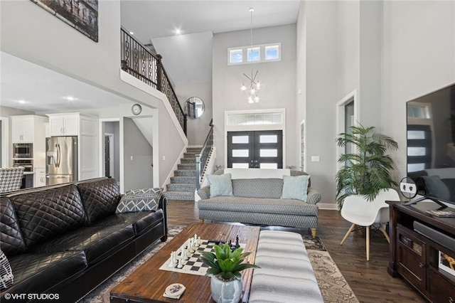 living area with stairs, a towering ceiling, baseboards, dark wood-type flooring, and a chandelier