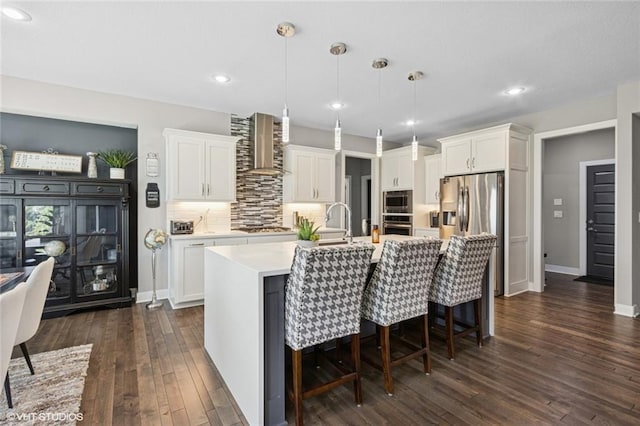 kitchen featuring wall chimney range hood, light countertops, stainless steel appliances, white cabinetry, and dark wood-type flooring