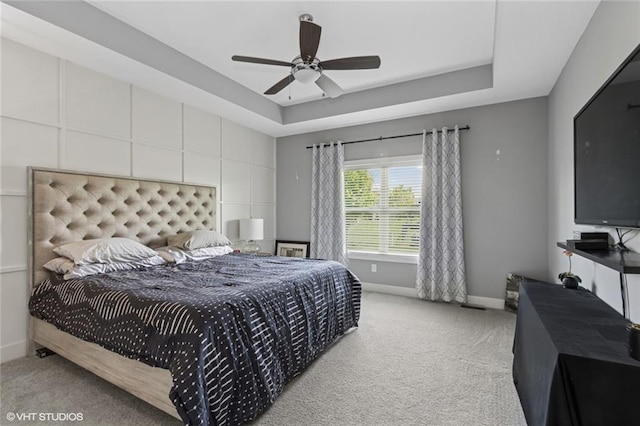 bedroom featuring a ceiling fan, baseboards, light carpet, and a tray ceiling