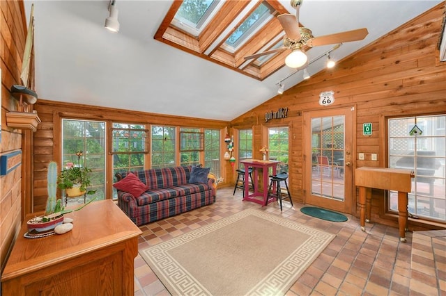 living room with track lighting, vaulted ceiling, wood walls, a skylight, and ceiling fan