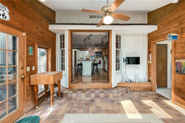 tiled foyer entrance featuring wood walls, a ceiling fan, and track lighting