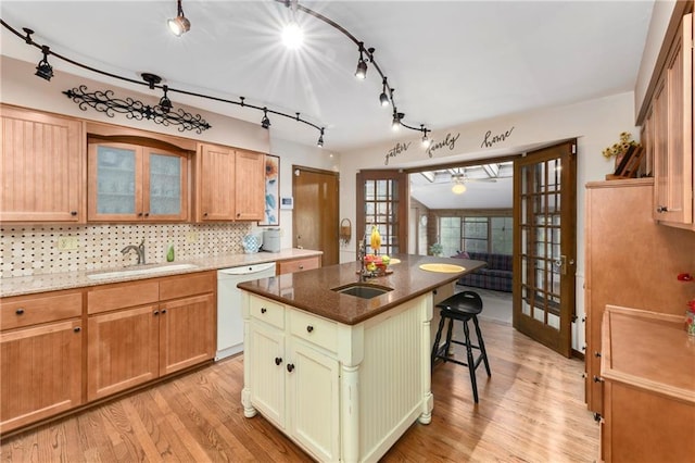 kitchen featuring white dishwasher, a sink, light wood-style floors, a breakfast bar, and tasteful backsplash