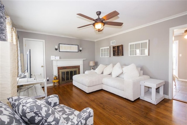 living area with a ceiling fan, wood finished floors, baseboards, ornamental molding, and a brick fireplace