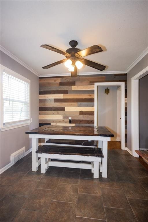 interior space featuring a ceiling fan, wood walls, crown molding, and visible vents