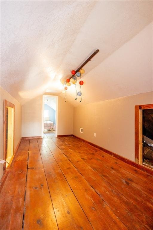 bonus room with vaulted ceiling, baseboards, a textured ceiling, and light wood-style floors