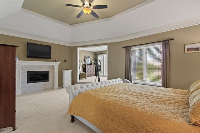 bedroom with carpet floors, ceiling fan, a tiled fireplace, and a raised ceiling