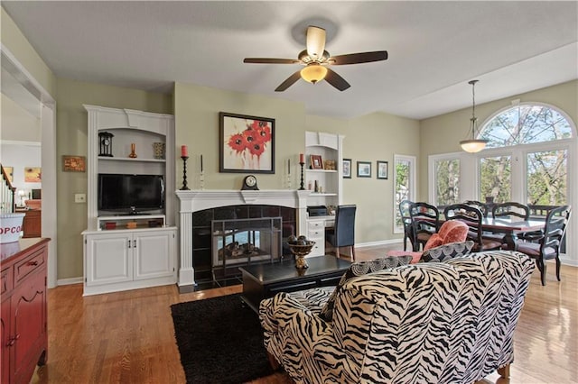 living room with a tiled fireplace, a ceiling fan, and light wood-style flooring