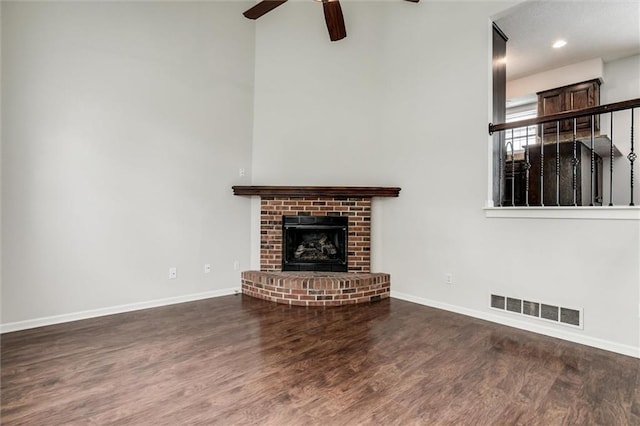 unfurnished living room featuring a brick fireplace, a ceiling fan, baseboards, wood finished floors, and visible vents