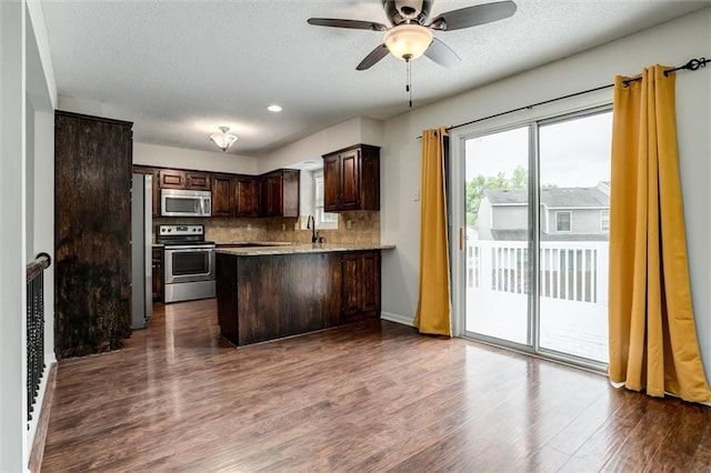 kitchen featuring a peninsula, dark brown cabinetry, dark wood-type flooring, a sink, and stainless steel appliances