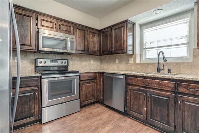 kitchen featuring dark brown cabinets, a textured ceiling, tasteful backsplash, light wood finished floors, and appliances with stainless steel finishes