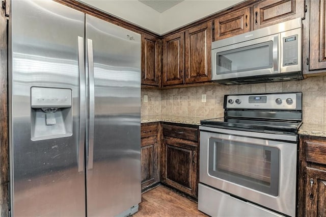 kitchen with dark brown cabinetry, appliances with stainless steel finishes, tasteful backsplash, light wood-type flooring, and light stone counters